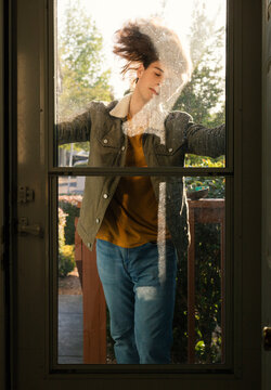 Androgynous Person flips hair behind glass storm door