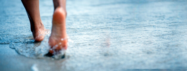 Woman bare foot walking on the summer beach. close up leg of young woman walking along wave of sea water and sand on the beach. Enjoyment barefoot walk outdoor with freedom. Relaxation Travel Concept.