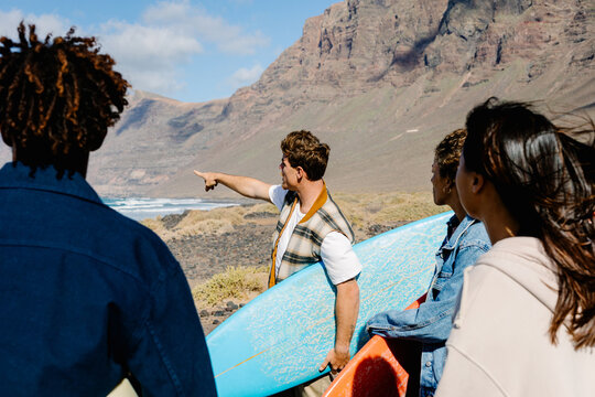 Diverse group of surfers spot big waves on the shore of a rocky beach