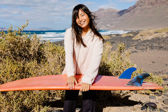 Portrait of a young Chinese woman happily posing with her surfboar