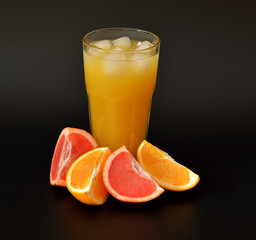 Citrus juice with ice on a black background, next to pieces of orange and grapefruit.