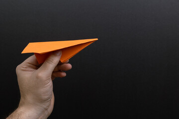 Hand holding an orange paper airplane on a black background. symbolizing creativity, imagination, and the spirit of adventure