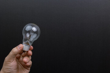 Hand holding a light bulb against a black background. Symbolizing: innovation, creativity, ideas, inspiration, potential.