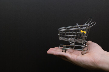 Hand holding a miniature shopping cart on a black background. Symbolizing e-commerce consultancy, commerce, convenience, consumerism, shopping.