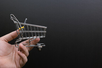 Hand holding a miniature shopping cart on a black background. Symbolizing e-commerce consultancy, commerce, convenience, consumerism, shopping.