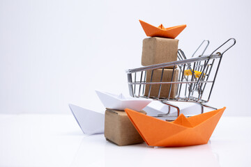 Shopping cart filled with boxes and paper boats on a white background.. Symbolizing e-commerce, modern commerce, sale and export.