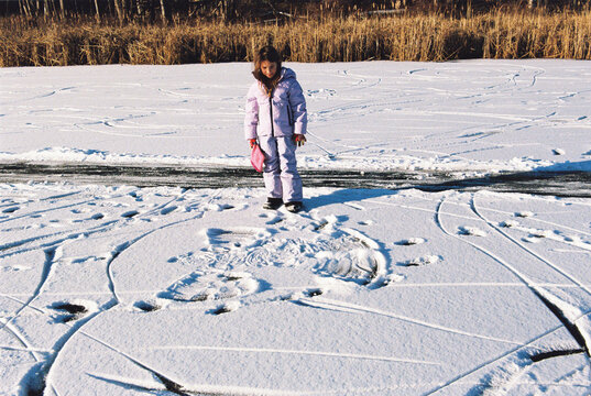 Child examines the snow angel she just made on a snow-covered pond