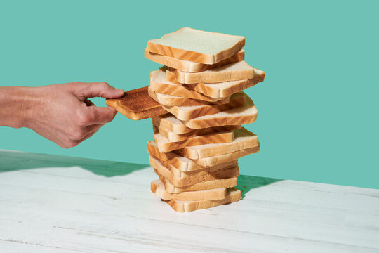 man taking a toast from of pile of untoasted slices of bread