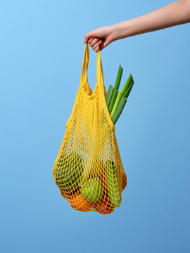 Hand Holding a Yellow Mesh Bag with Fresh Vegetables