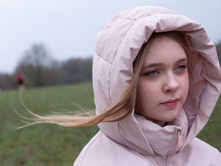 Outdoor portrait of tween girl in pink coat on windy day.