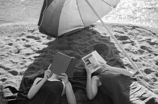 Two Young women reading books on the beach under a sun umbrella