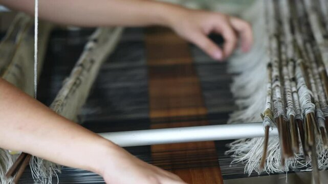 Close-up of woman's hands weaving yarn, silk thread and woven by using mechanic wooden machine to weave. Weaving and traditional crafts.