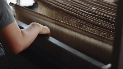 Close-up of woman's hands weaving yarn, silk thread and woven by using mechanic wooden machine to weave. Weaving and traditional crafts.