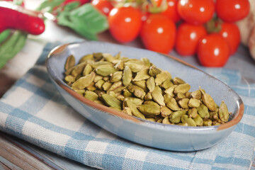 Green cardamom pods are arranged in a bowl alongside ripe tomatoes