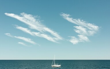 Fototapeta premium Small sailboat on calm blue sea under a pale blue sky with wispy clouds. Tranquil seascape, minimalist composition