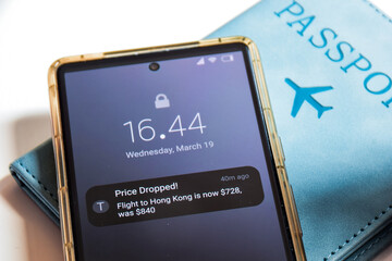 Real-time Push notifications with plane ticket price drop alert on mobile screen with passport on the desk. Track and compare flight prices concept. 