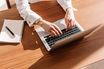 Hands typing on laptop at modern workspace with notebook and pen