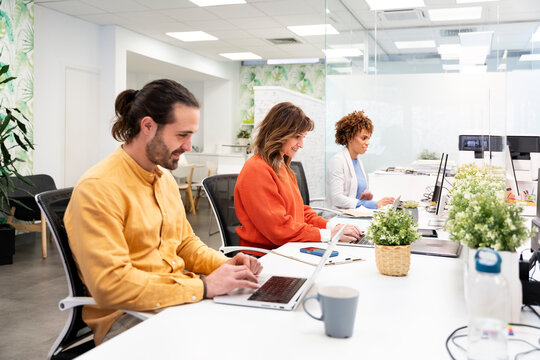 Office workers typing on laptops, working together in modern office