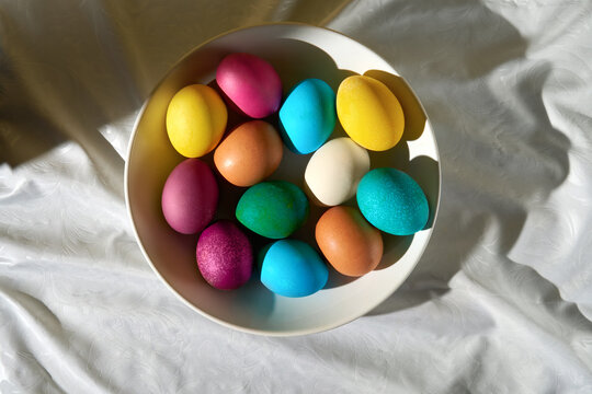 Easter eggs in a bowl on a soft white fabric backdrop in sunlight