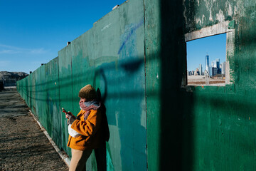 Woman leaning against green fence with New York city skyline view
