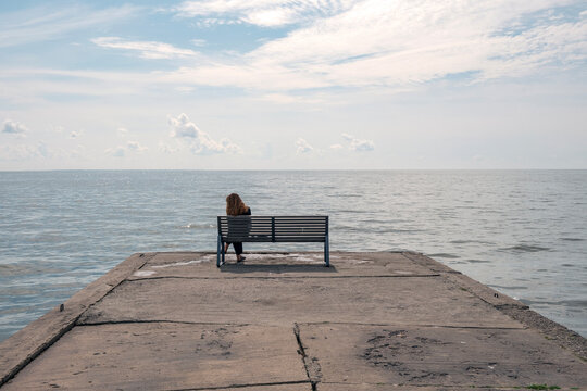 Lonely woman sitting on pier bench at seafront