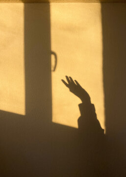 Shadow of a hand reaching towards a window in warm golden light 
