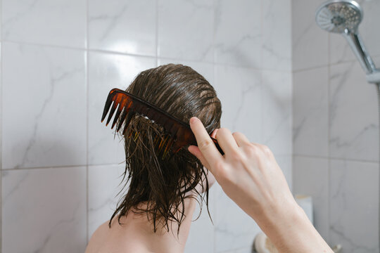 Young man combing wet hair in shower