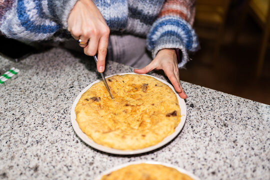 Woman slicing spanish omelette with knife on white plate