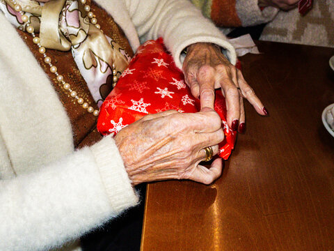 Elderly woman opening christmas gift at home