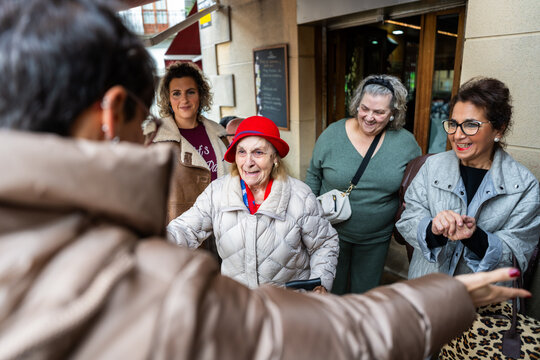 Family welcoming elderly woman with open arms in front of restaurant