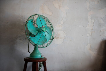 Vintage Teal Fan on Wooden Stool against Rustic Wall