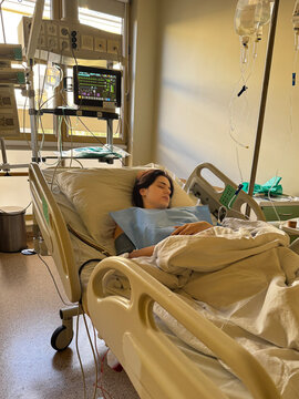 A young woman lies in a hospital bed in an intensive care unit