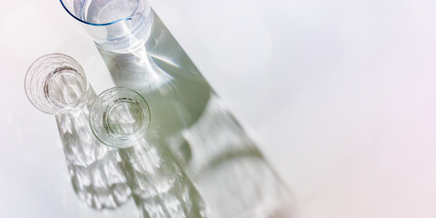 Water Glass with shadows at sunlight on white, delicate pale color, minimal aesthetic top view shiny glasses at natural light, summer drink concept, pastel gradient interplay light and shadow