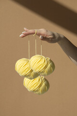 Three yellow balls of knitting thread hang on a woman's beautifully manicured fingers. Wool skeins with yarn on a light brown background in sunlight.