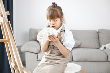 Girl with Down syndrome wearing beige apron painting on an easel