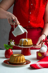 A woman in a red dress pours cream over the Easter cake.