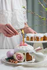 A woman in a white dress lights a candle on an Easter cake.
