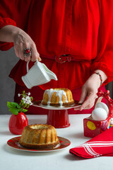 A woman in a red dress pours cream over the Easter cake.