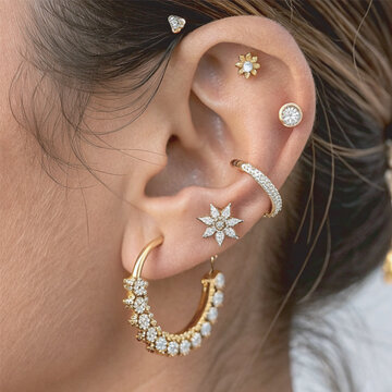 A close-up of a beautifully adorned ear featuring multiple elegant piercings with gold and diamond jewelr for National Piercing Day
