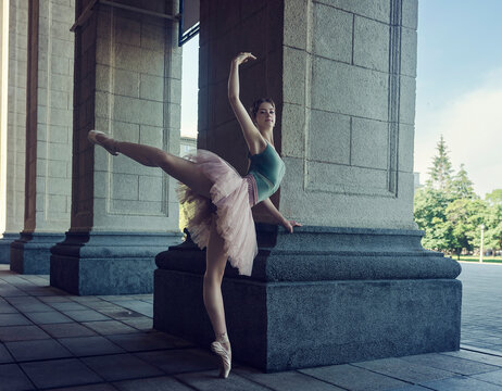 ballerina in tutu and pointe shoes shows ballet elements on the streets on a sunny summer day