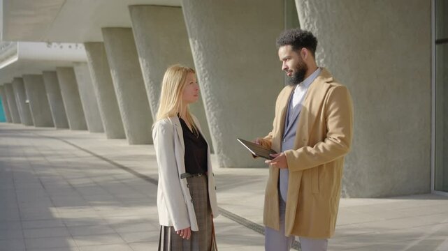 Businesswoman and businessman are having a dynamic conversation outdoors, man showing to his coligue graphs on the tablet, business backdrop that emphasizes collaboration and innovation in careers