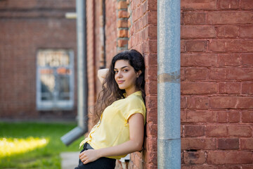 Young adult beautiful brunette girl in casual clothes on the background of a building with red brick walls
