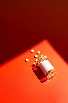 Spilled pills from a medicine bottle on red background
