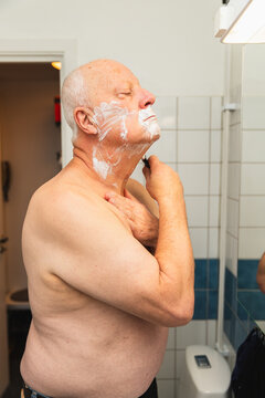Senior pensioner shaving his face at home in the bathroom