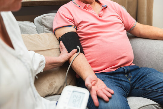 Senior woman helping husband measure blood pressure on sofa - Powered by Adobe