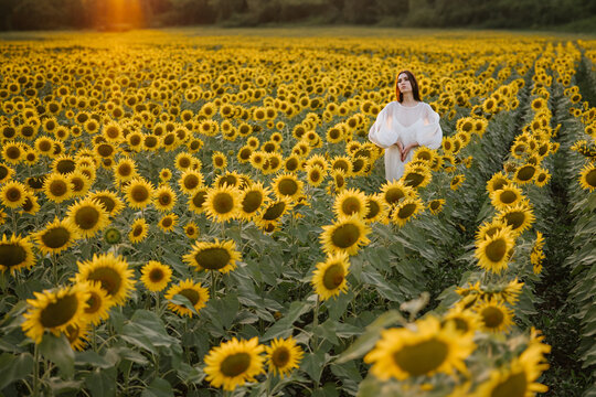 A girl walking in a field of sunflowers at sunset