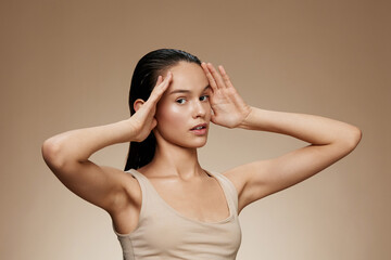 Fototapeta premium Young female model with long hair striking a serene pose against a warm brown background, conveying calmness and mindfulness, ideal for wellness concepts