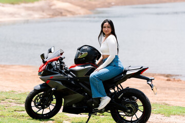 Obraz premium Young woman relaxing on her sport motorcycle by a serene lake, embracing the thrill of adventure and the essence of freedom