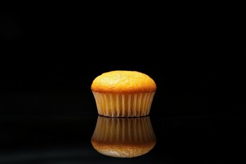 A single golden muffin rests on a reflective black surface
