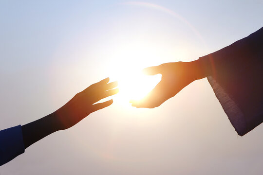 Hand of salvation, Christian hand reaching out to the hand of Jesus Christ, bright sun silhouette
